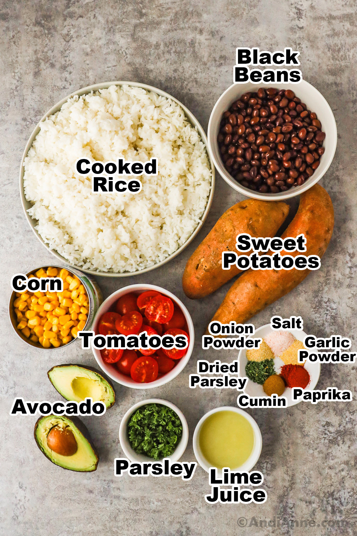 Recipe ingredients including bowls of rice, black beans, tomatoes, parsley, lime, canned corn, sliced avocado and bowl of spices.