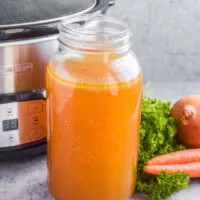 A large mason jar with broth and slow cooker in background.