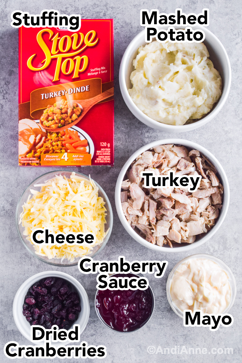 Recipe ingredients on counter including box of stove top stuffing, bowl of mashed potatoes, bowl of turkey, bowl of shredded cheese, bowl of mayonnaise, cranberry sauce and dried cranberries.