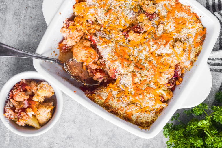 Baked cheese cauliflower casserole in square dish with serving scooped out into a white bowl.