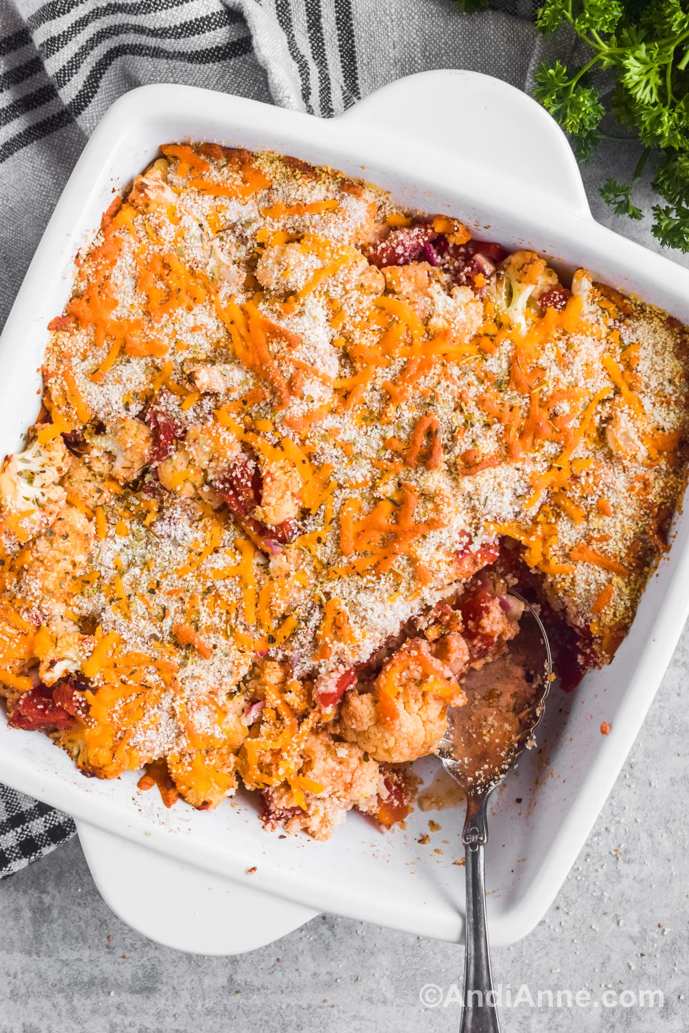 Baked cauliflower casserole recipe in a white square dish with a spoon in the bottom corner.