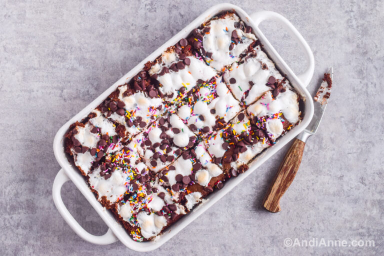 Sliced dessert with melted marshmallows and chocolate on top. A small knife is beside the baking dish.
