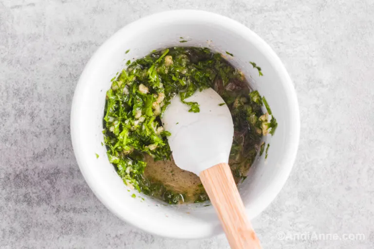 Small white bowl with chopped parsley, oil, minced garlic, salt and pepper. A spatula inside.