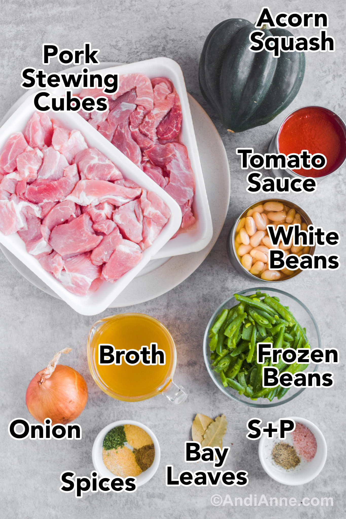 Recipe ingredients on a counter including two packages of raw pork stewing cubes, acorn squash, can of tomato sauce, canned white beans, bowl of frozen beans, glass container of broth, onion and spices.