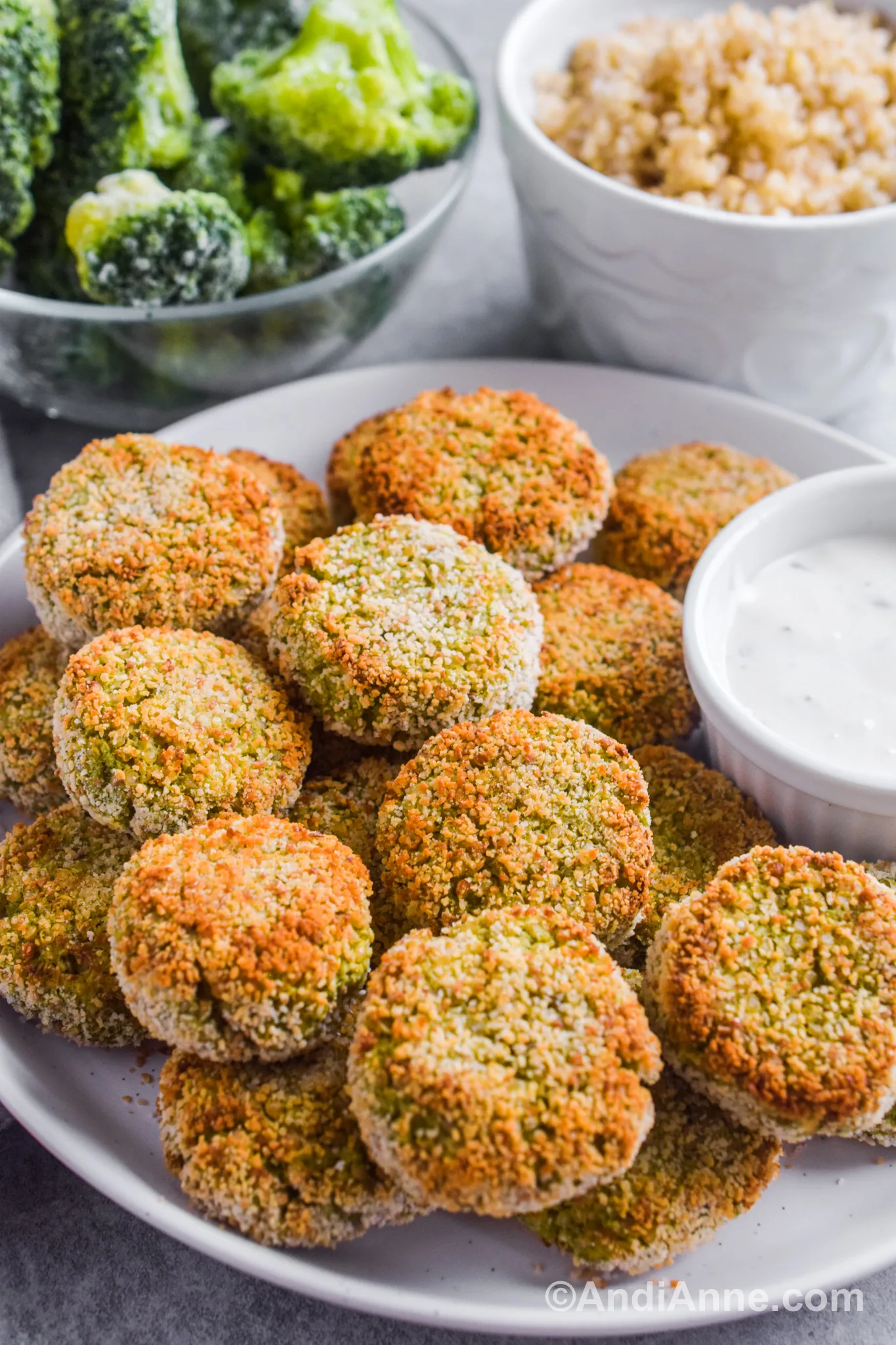 A plate of broccoli quinoa nuggets with ranch dressing on the side. Bowl of frozen broccoli and bowl of quinoa are behind the plate.