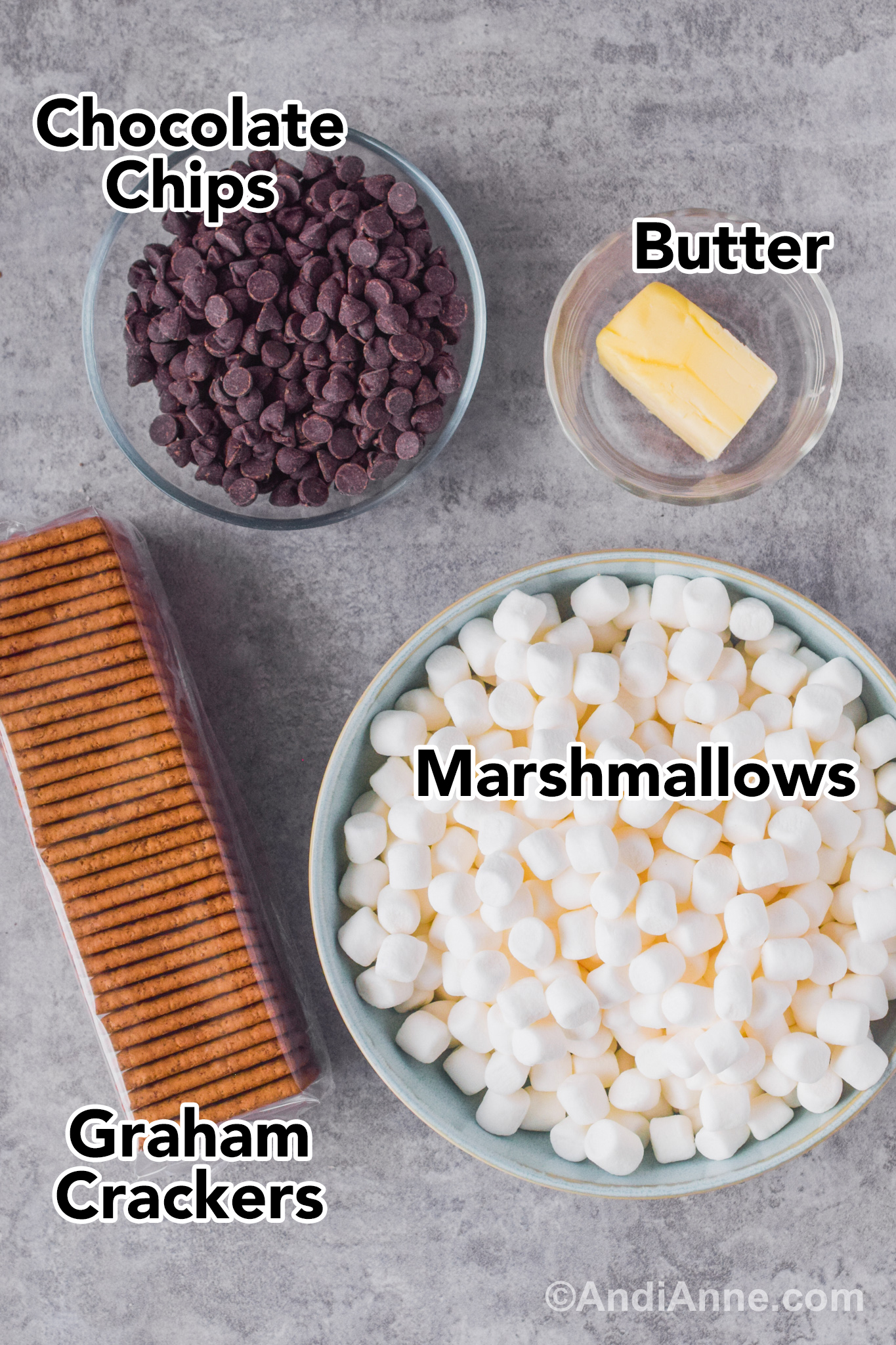 Bowl of chocolate chips, bowl of mini marshmallows, bowl of butter and sleeve of graham crackers on a counter.