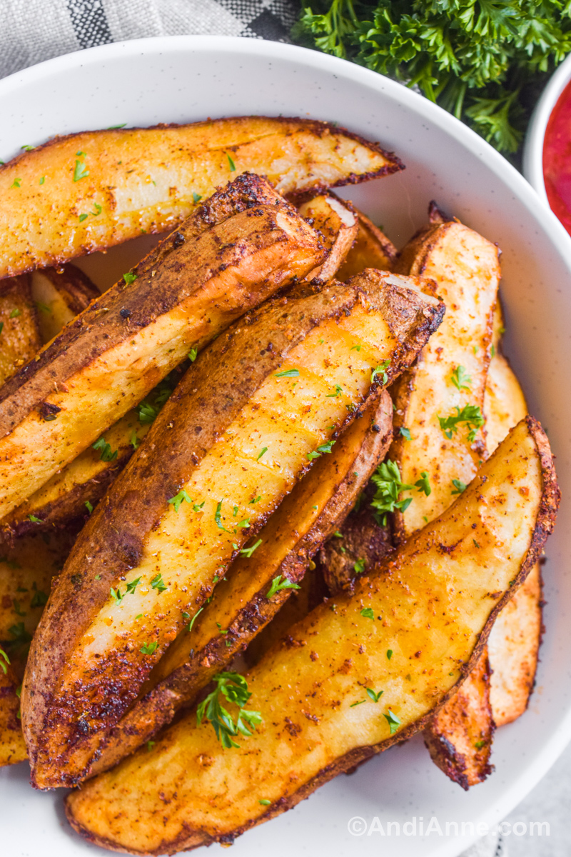 Crispy potato wedges on a white plate with chopped parsley sprinkled on top.