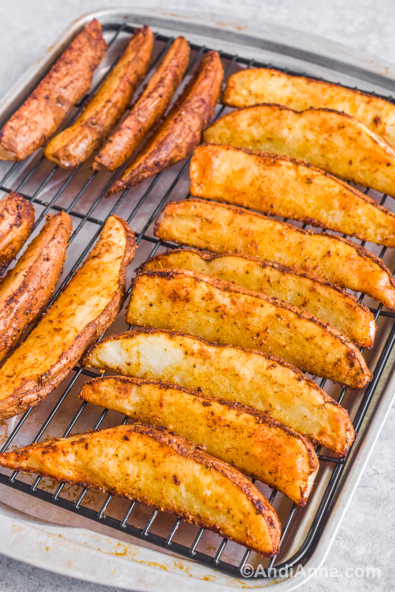 Close up of cooked potato wedges on a baking rack (rack with baking sheet underneath) and seasoned with spices.