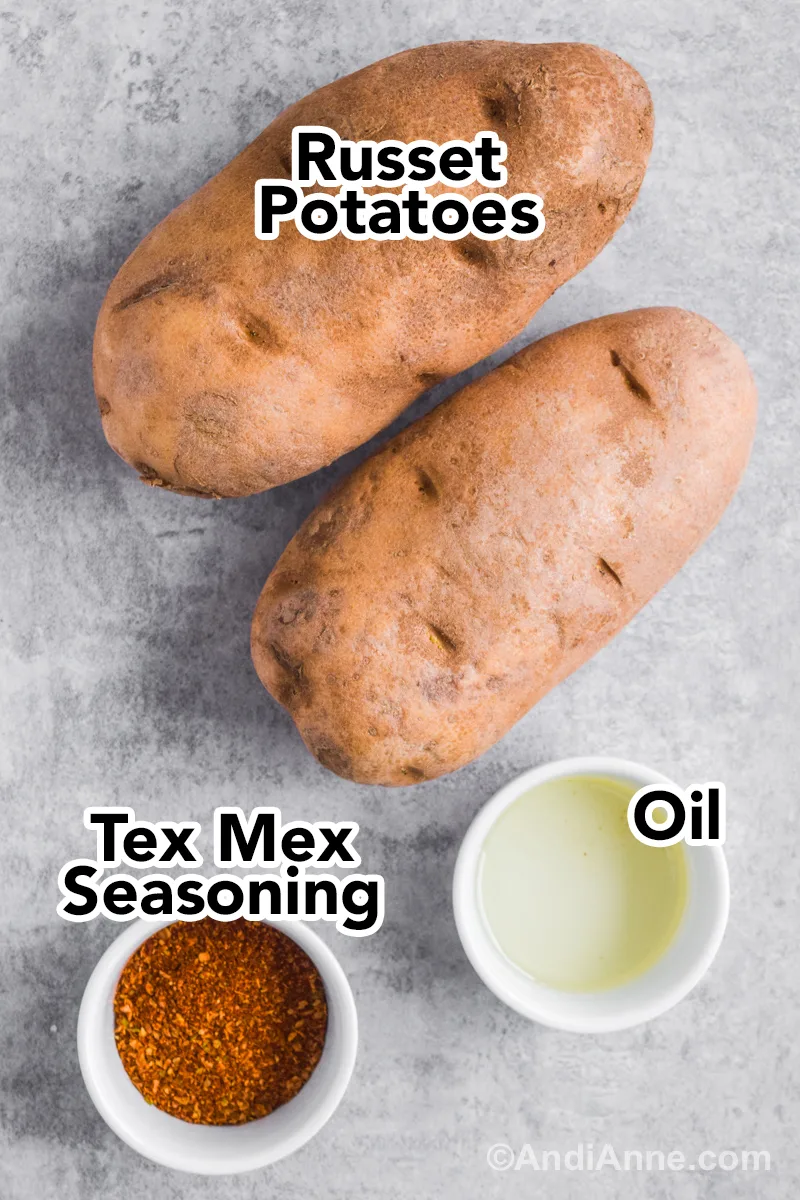 Recipe ingredients on the counter including two russet potatoes, tex mex seasoning and oil in small bowls.