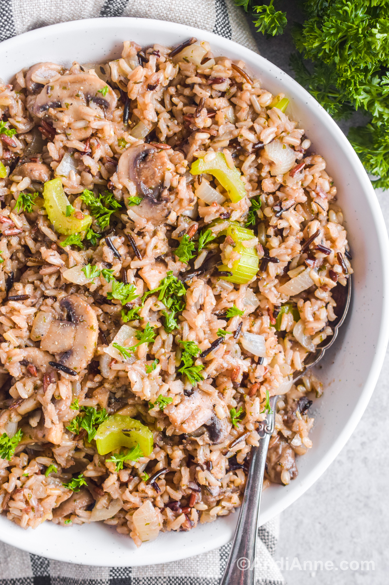 Wild rice and brown rice with chopped mushroom, and celery in a bowl with a spoon.