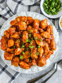 A plated of sweet and sour chicken bites over a bed of rice and chopped green onion on top