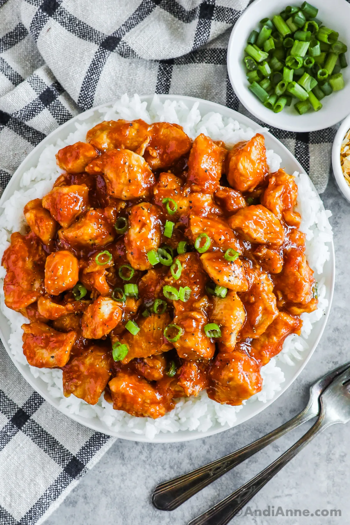 A plated with saucy sweet and sour chicken bites over rice and topped with chopped green onion.