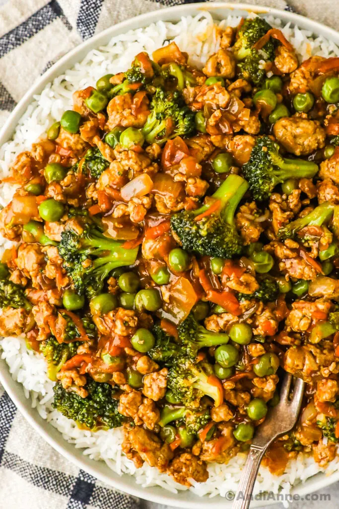 A plate with teriyaki ground turkey, broccoli and peas on a bed of white rice