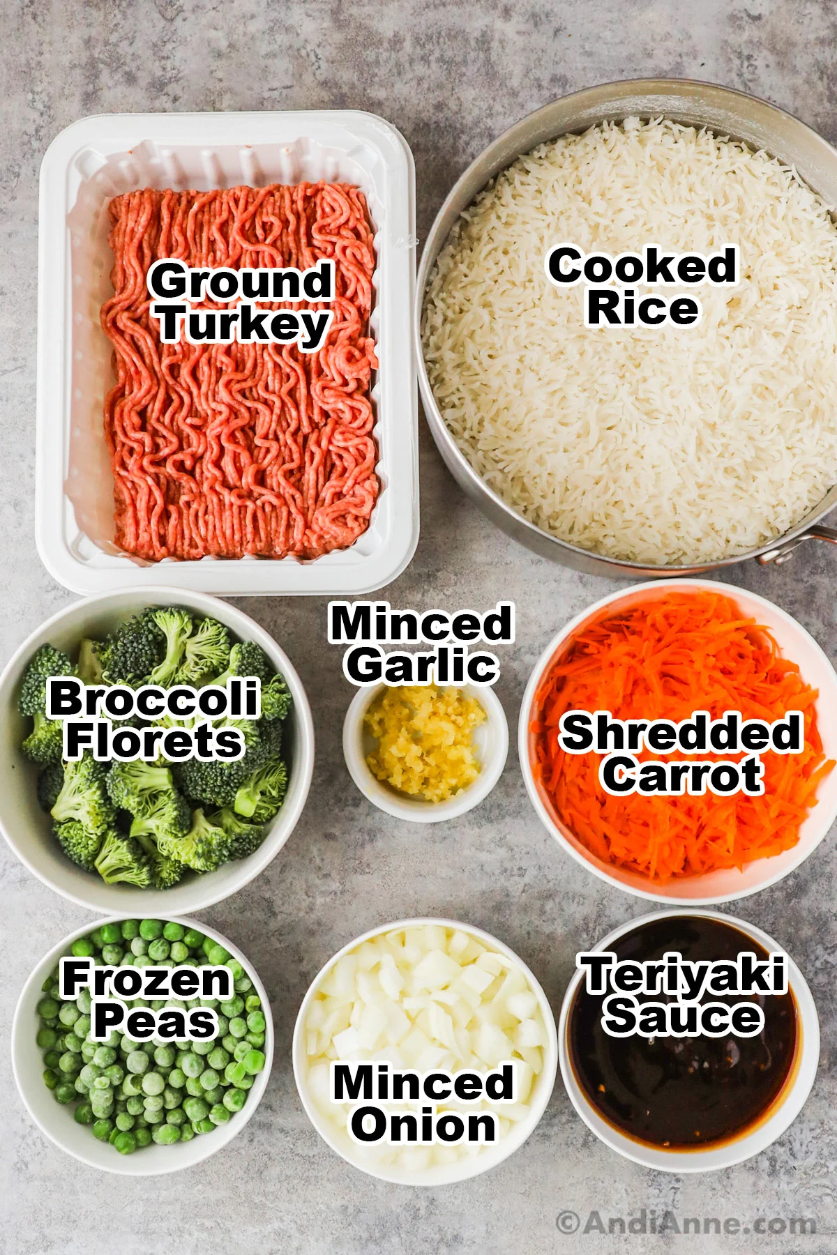 Recipe ingredients including a pot of white rice, container of raw ground turkey, bowls of broccoli florets, minced garlic, shredded carrot, frozen peas, minced onion and teriyaki sauce.