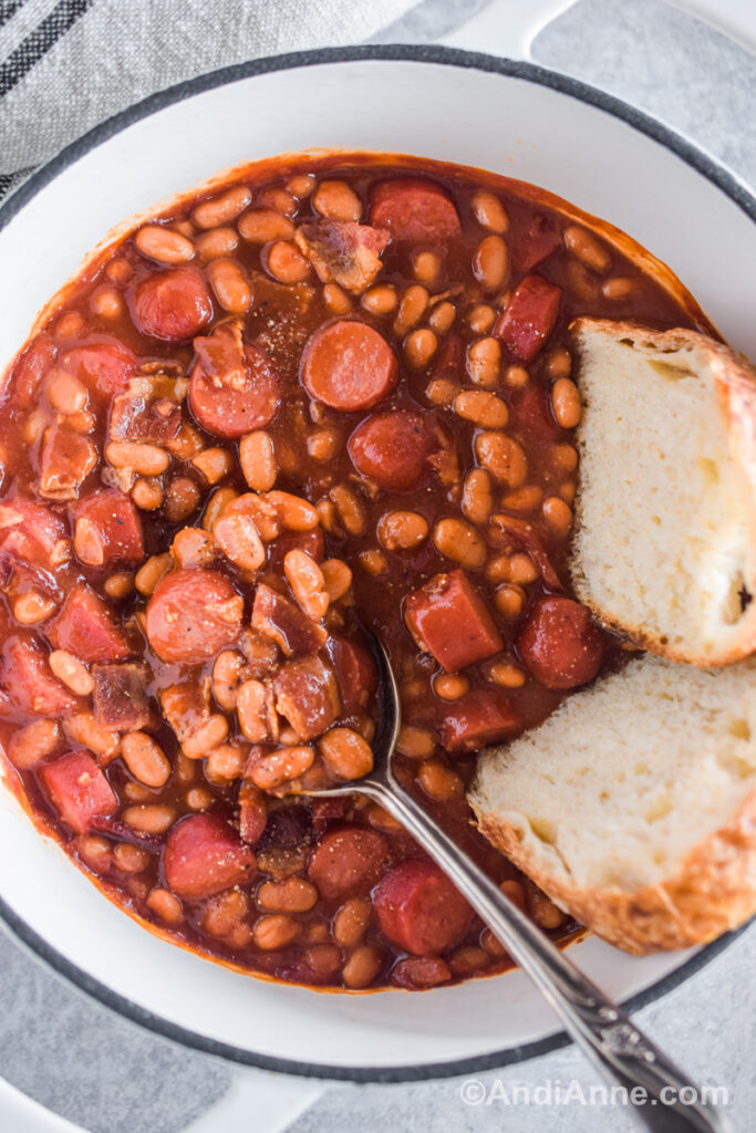 Overhead view of beans and franks in a bowl with bread.