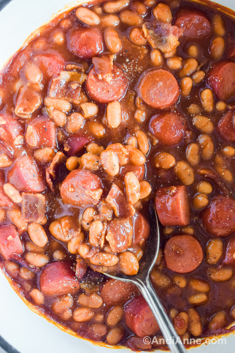 Close up of wieners and beans in sauce with a spoon.