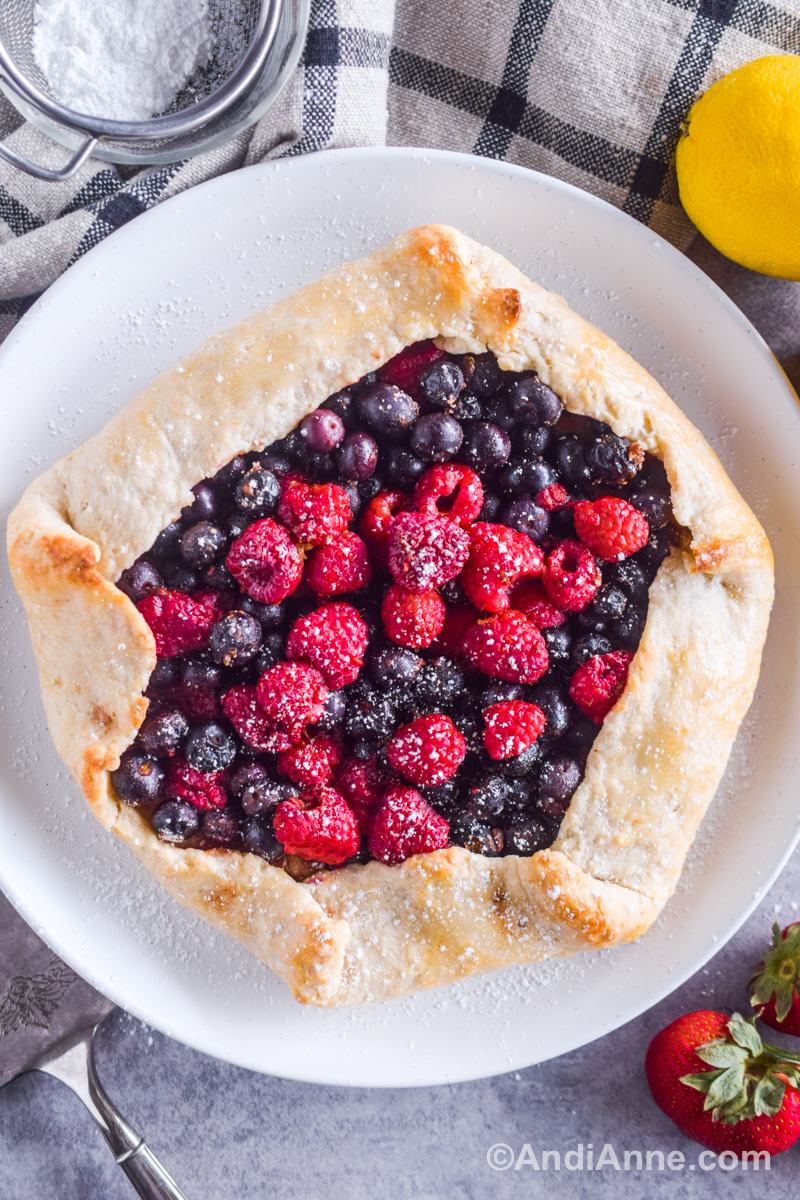 A berry fold over pie stacked with raspberries and blueberries on a plate sprinkled with powdered sugar.