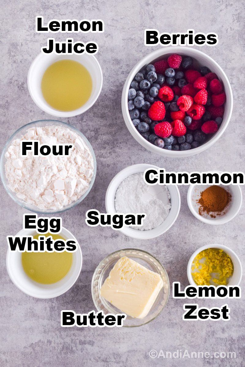 Recipe ingredients on a counter including bowls of lemon juice, berries, flour, cinnamon, powdered sugar, egg whites, cold butter and lemon zest.