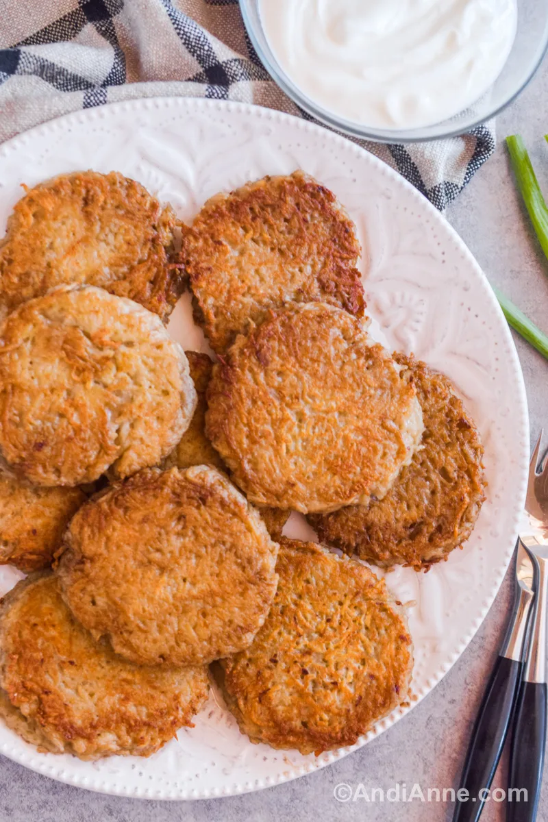 German potato pancakes (kartoffelpuffer) on a white plate with a bowl of yogurt beside it.