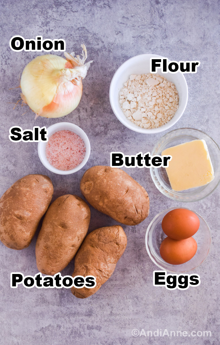 Recipe ingredients on a counter including four russet potatoes, bowl of flour, salt and butter, eggs and an onion.