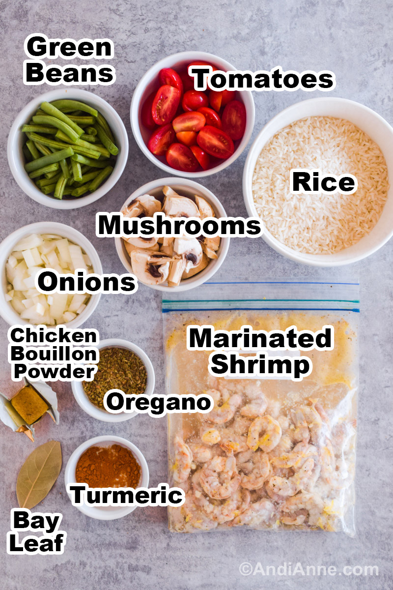 Recipe ingredients on the counter including small white bowls of chopped green beans, cherry tomatoes, mushrooms, onion, rice, oregano and turmeric powder. A bag with raw shrimp in a marinated sauce is also there.