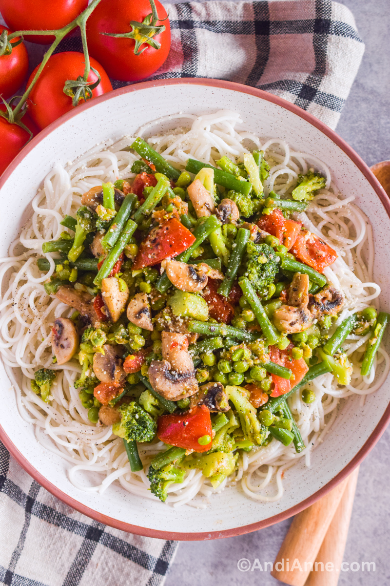 Cooked vegetables including green beans, mushrooms, tomatoes and peas, all sprinkled with parmesan cheese and served over spaghetti pasta noodles in a large bowl.
