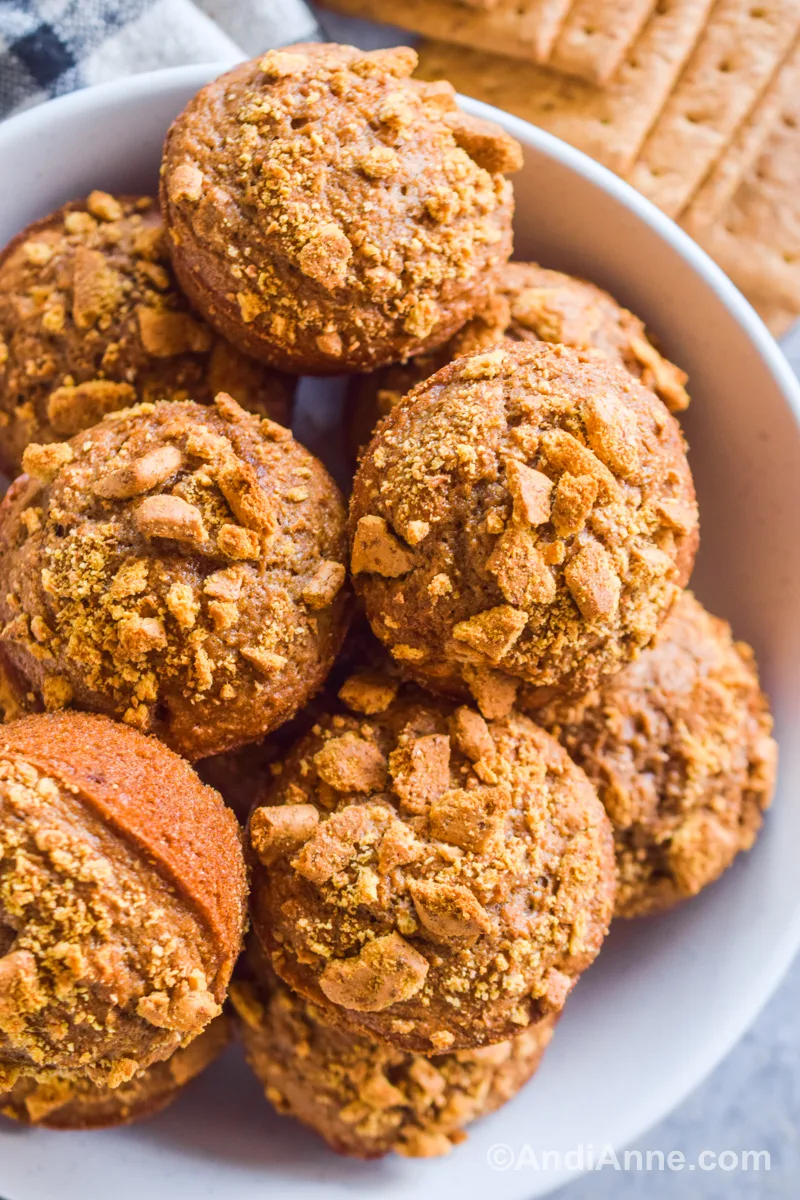 A pile of muffins with graham cracker toppings in a white bowl, with graham crackers beside the bowl.