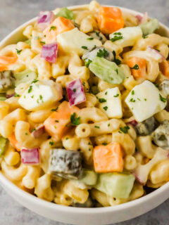 A bowl of creamy macaroni salad with celery, pickles, and eggs
