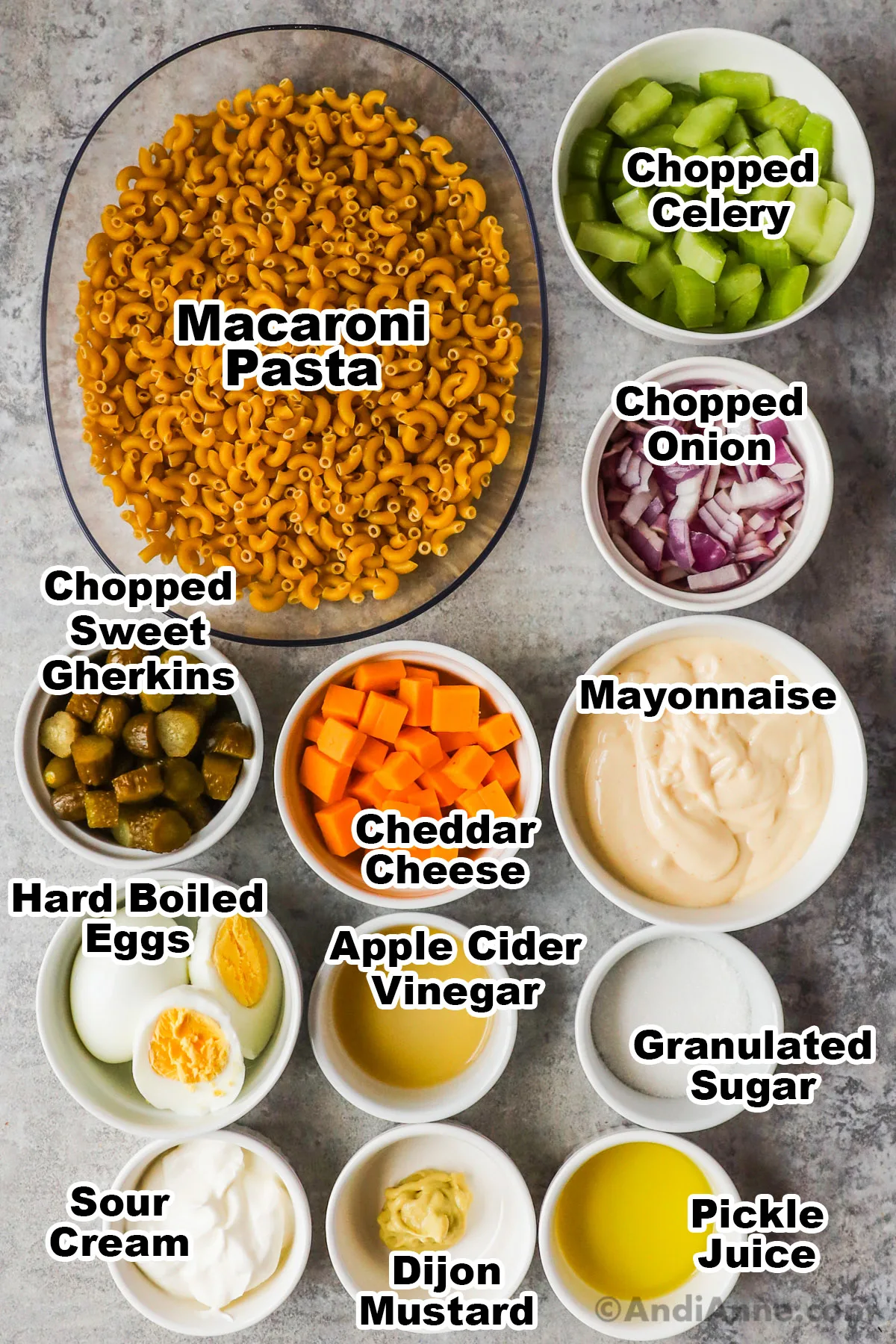 Recipe ingredients in bowls including chopped celery, onion, pickles, cheese, mayonnaise, macaroni pasta, hard boiled eggs, sour cream, sugar and pickle juice.