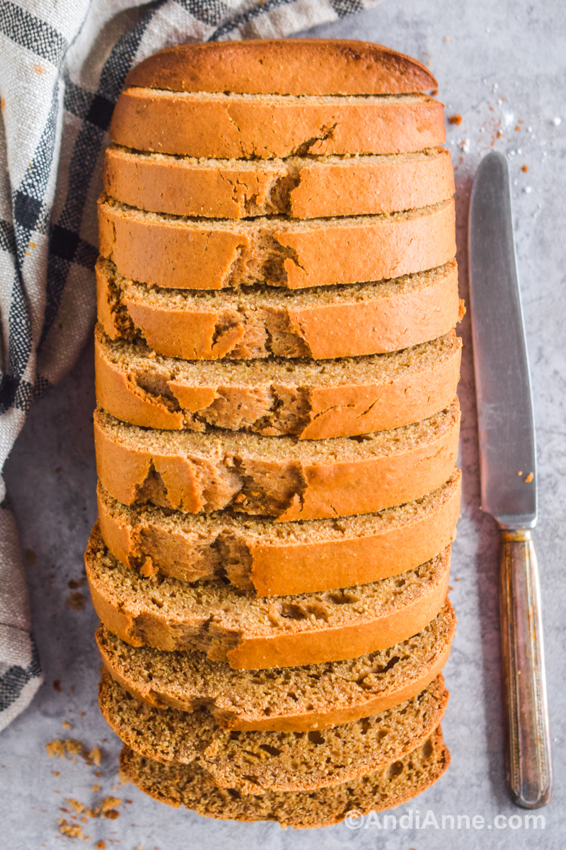 Looking down at the peanut butter bread cut into slices but stacked together. A bread knife and a kitchen towel surround the bread.