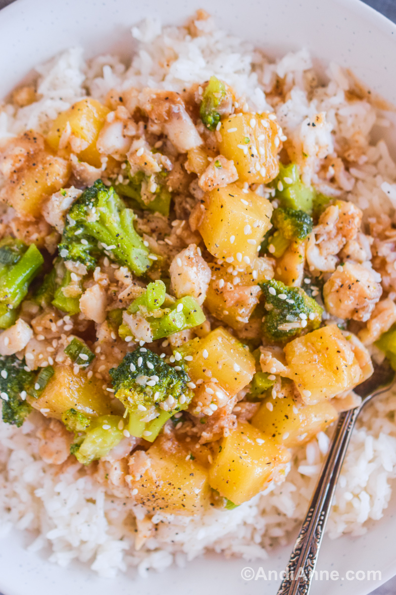 Pineapple chunks, broccoli florets, and chunks of fish in a sweet and sour sauce with sesame seeds over a bed of rice.