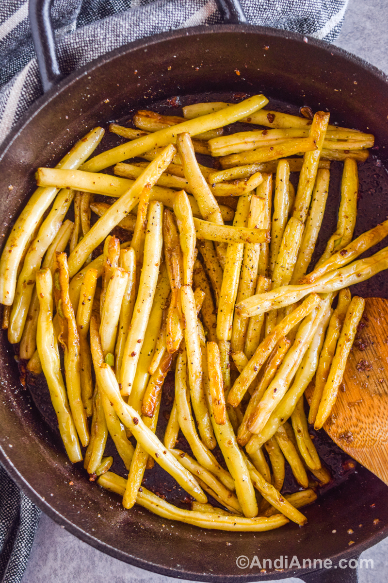 Cooked yellow beans with golden brown edges in a black skillet.