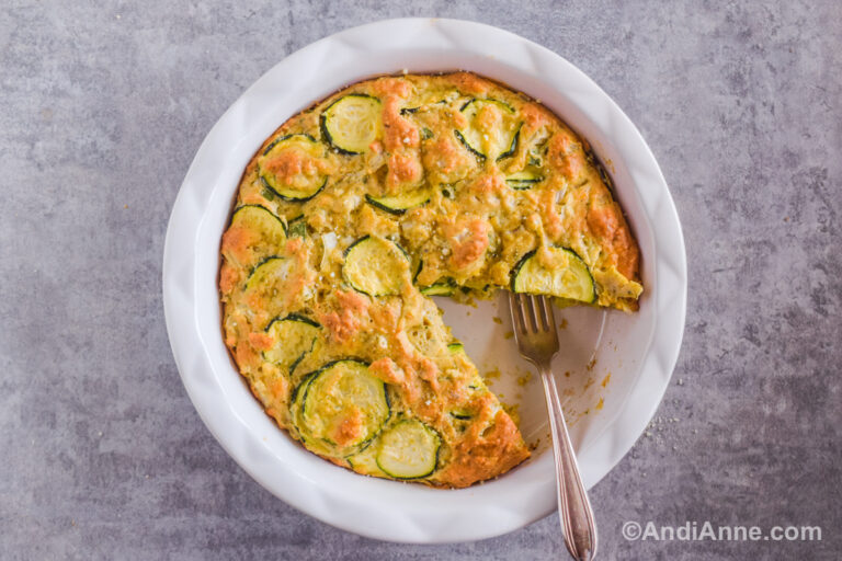 Baked zucchini pie in a white pie plate with a slice cut out and a fork inside.
