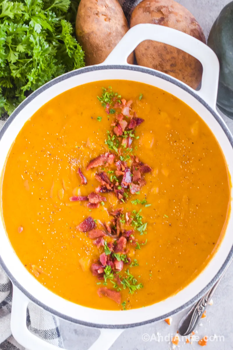 A large white pot with bacon squash soup. Chopped bacon and parsley sprinkled on top.