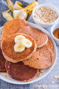Overhead view of stacked pancakes on a plate with banana slices on top.