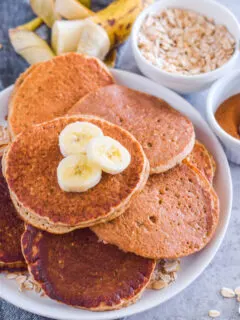 Overhead view of stacked pancakes on a plate with banana slices on top.