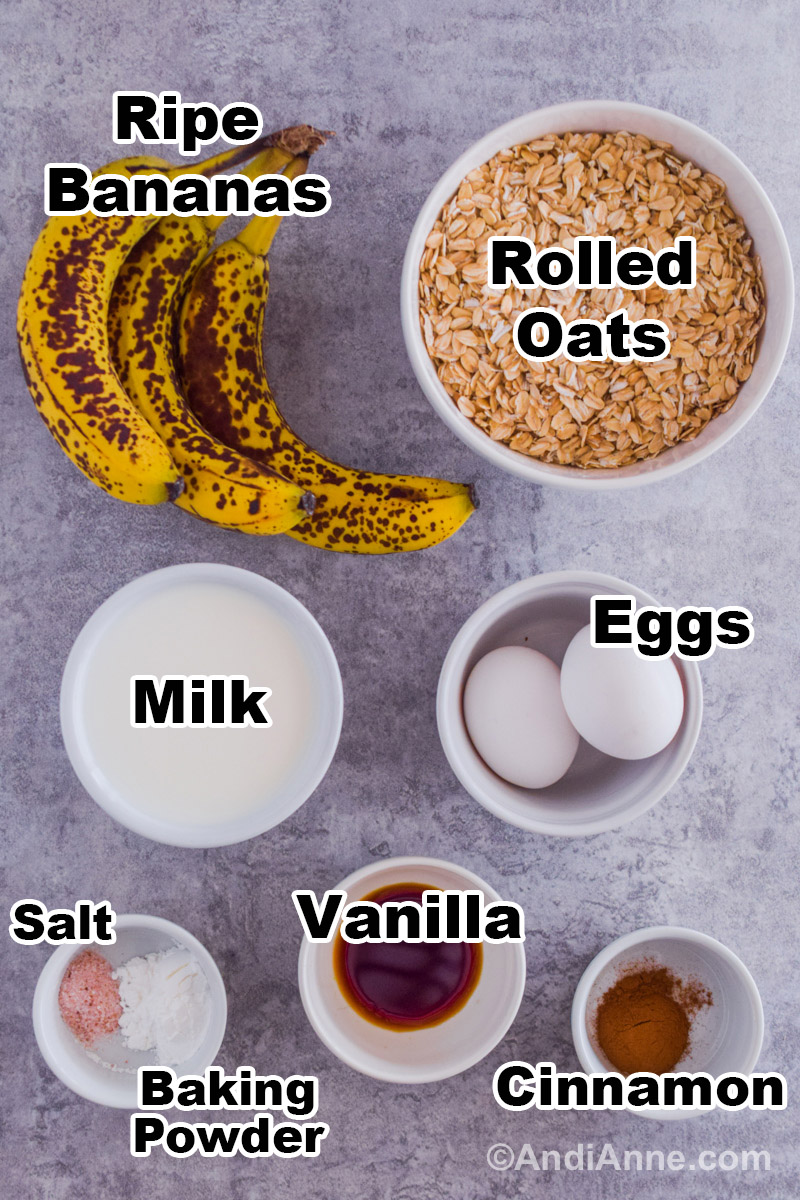 Recipe ingredients on the counter with a white bowl of rolled oats, ripe bananas, eggs, milk, vanilla, salt, baking powder and cinnamon.