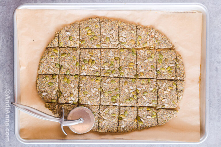 A baking sheet with the baked cracker seed dough sliced into squares and a pizza cutter.