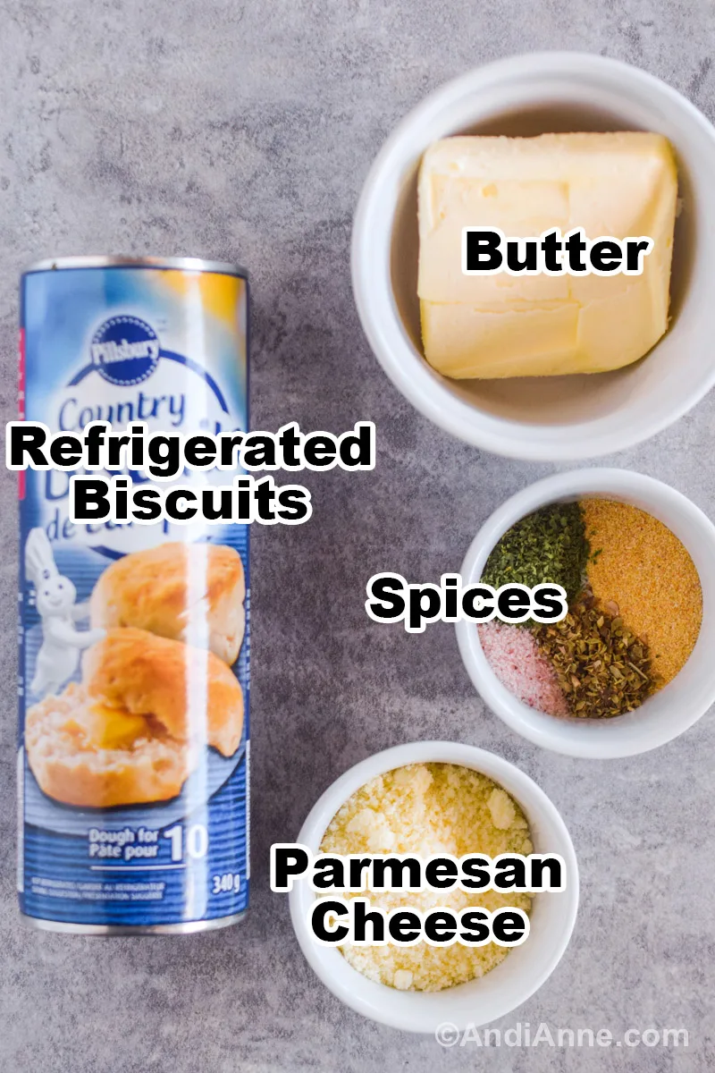 Recipe ingredients on counter including bowl of butter, bowl of spices, refrigerated biscuits, and bowl of parmesan cheese.