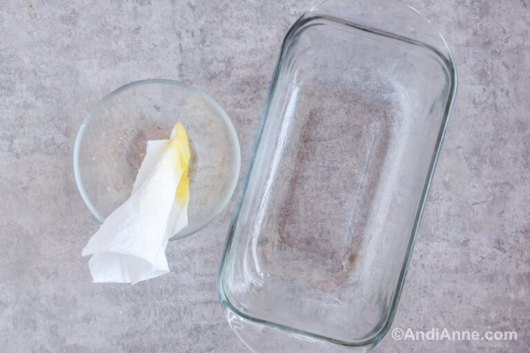 A bowl with a paper towel dipped in oil beside a glass loaf pan.