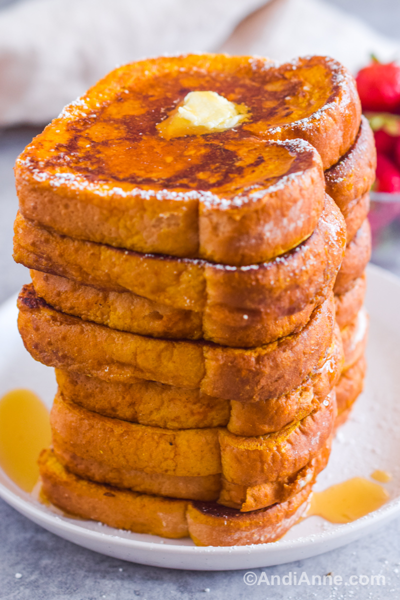A giant pile of all the cooked french toast stacked on top of each other. Drizzled with maple syrup, butter and powdered icing sugar.