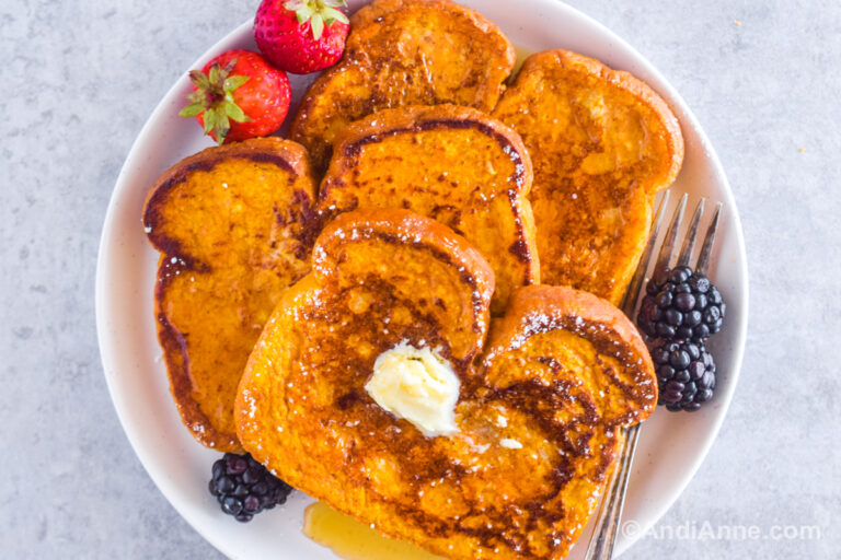 Three pumpkin french toast slices on a plate with fresh berries. Topped with butter and drizzled with maple syrup.