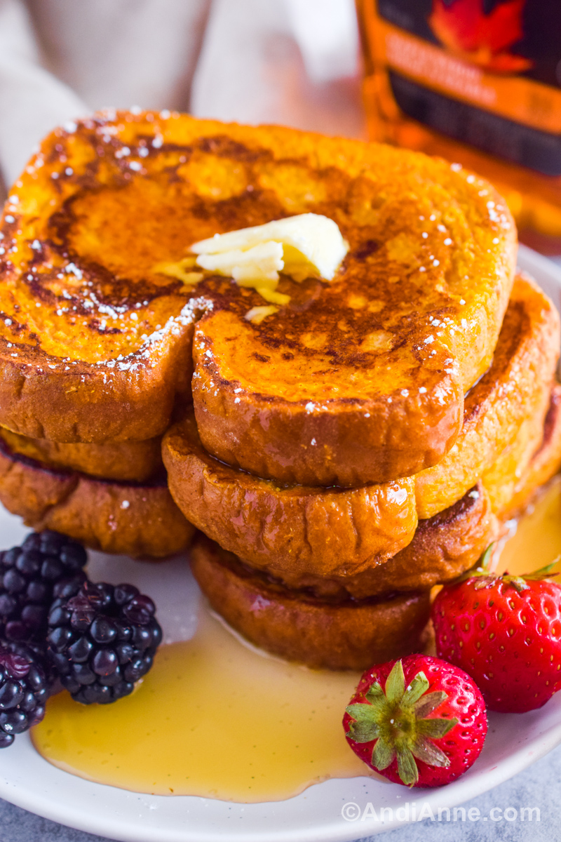 A stack of pumpkin french toast on a plate, drizzled with maple syrup and a few fresh berries.