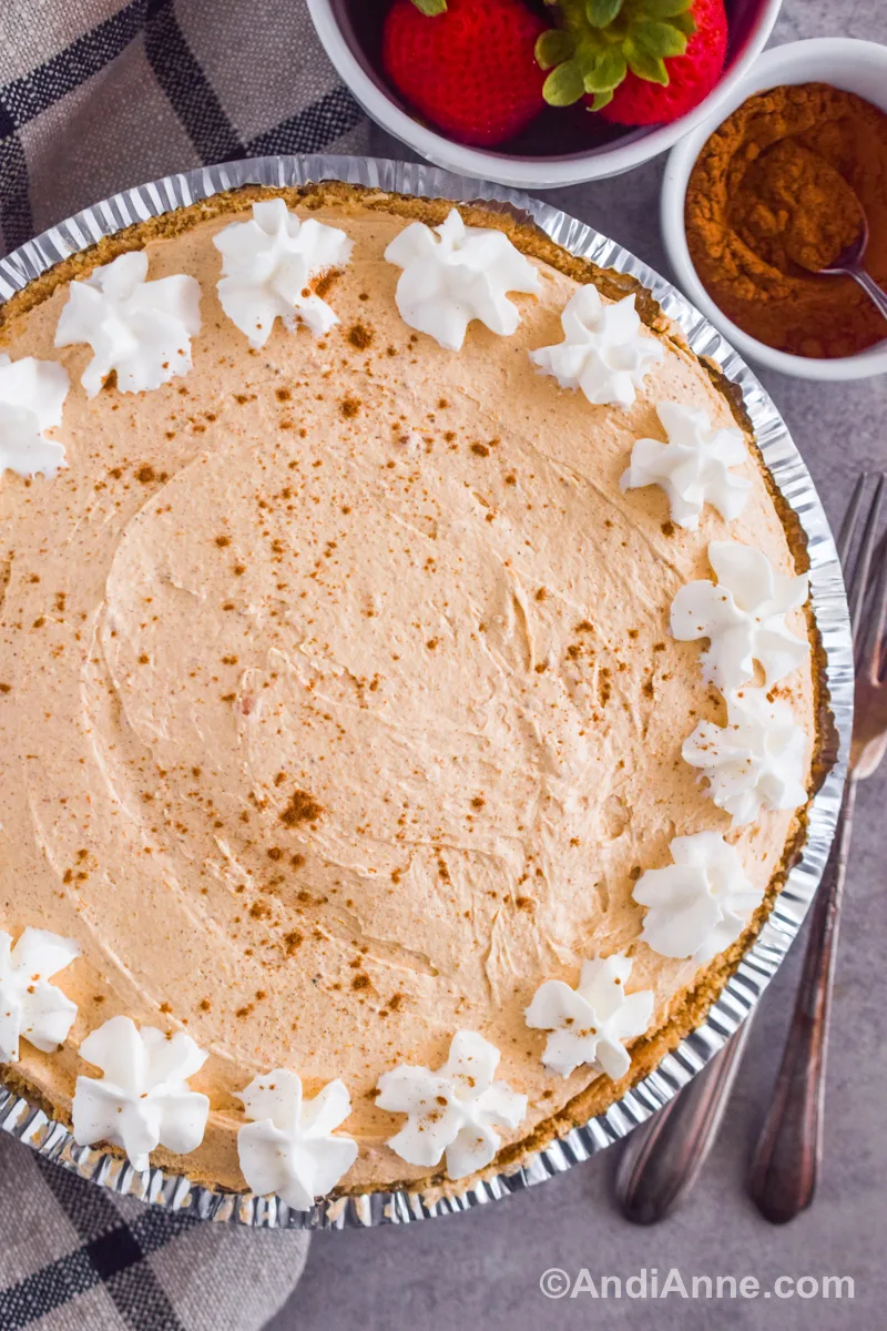 Looking down at pumpkin marshmallow pie with forks, a bowl of cinnamon and strawberries beside it.