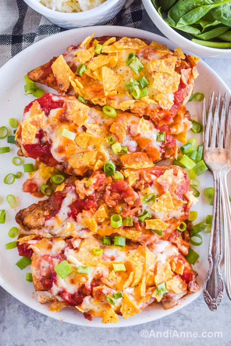 Baked salsa mozzarella chicken on a white serving plate with forks and chopped green onion sprinkled around.
