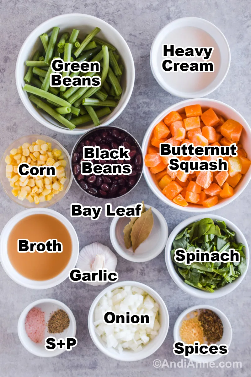 Recipe ingredients on a counter including bowls of green beans, bowl of butternut squash, bowl of cream, corn, black beans, broth, spinach, onion, and spices.