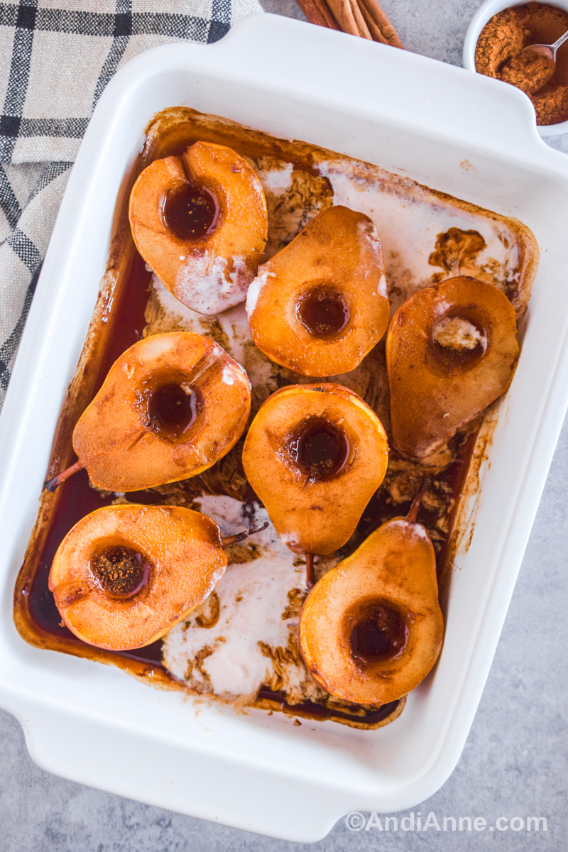 A white baking dish with baked sliced pears, brown sauce, and melted vanilla ice cream. 