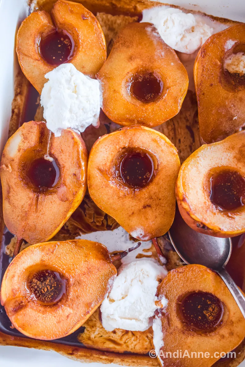 Close up of baked pears with brown syrup and scoops of vanilla ice cream, and a spoon.