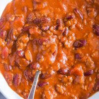 Chili recipe in a white bowl with a spoon inside.