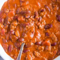 Chili recipe in a white bowl with a spoon inside.